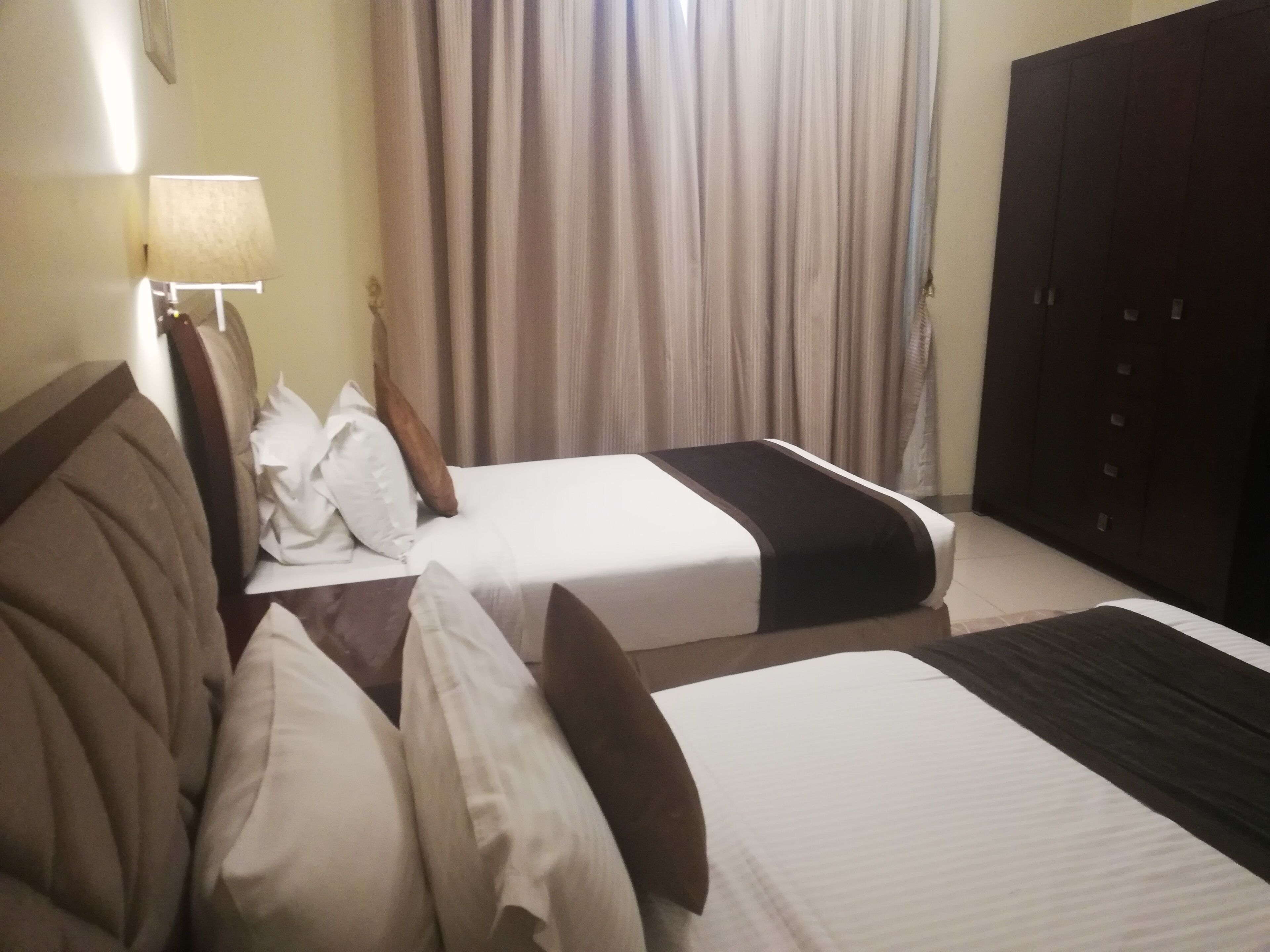A hotel room with two beds, a wardrobe, a lamp, and curtains.