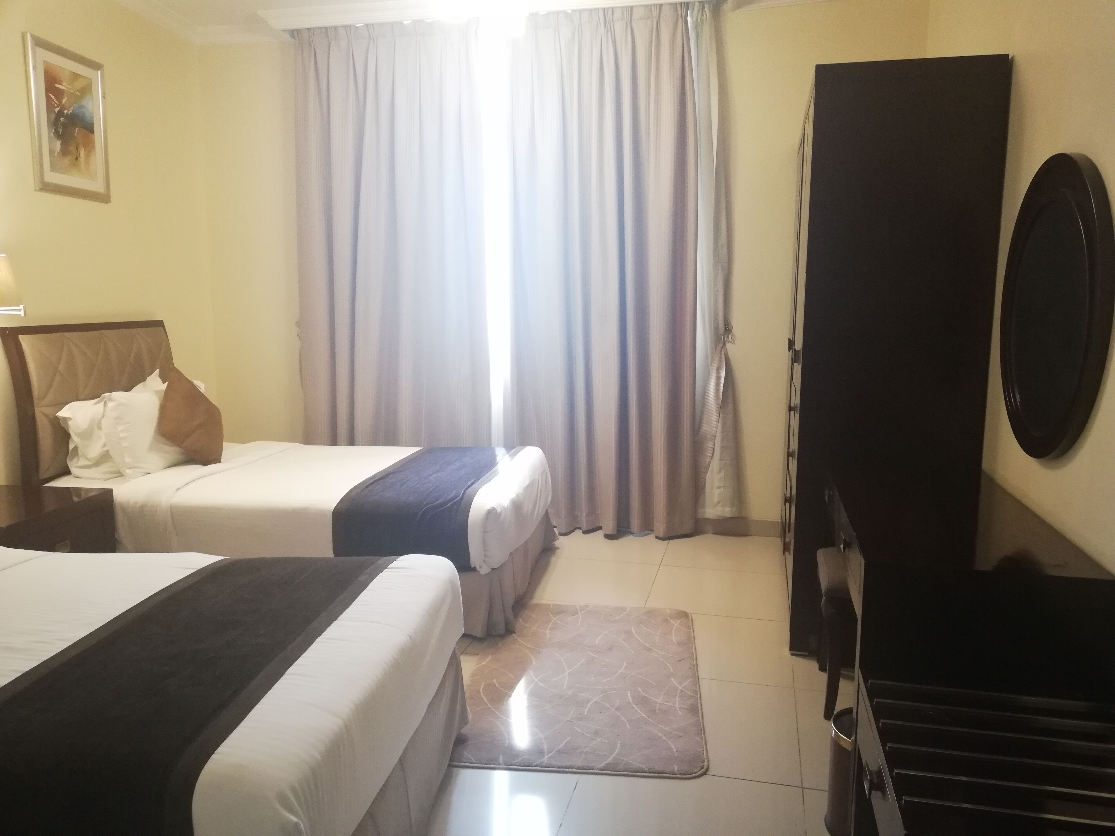A hotel room with two beds, a large mirror, a wardrobe, and a window with curtains.