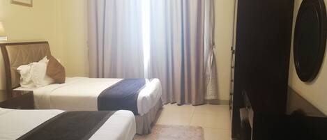 A hotel room with two beds, a large mirror, a wardrobe, and a window with curtains.