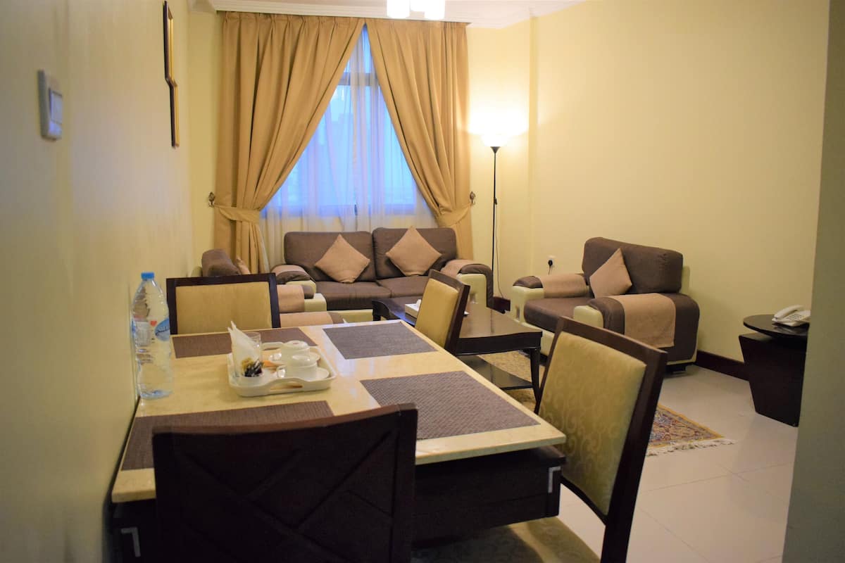 Habitación de hotel con una mesa de comedor, sillas, un sofá y una mesita de noche con lámpara.