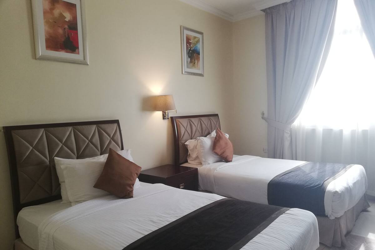 Una habitación de hotel con dos camas, cada una con cabecero, mesita de noche y lámpara.