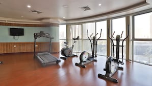 A spacious gym with various exercise equipment, large windows, and a flat-screen TV on the wall. - Crown Palace Hotel Ajman (Ajman)
