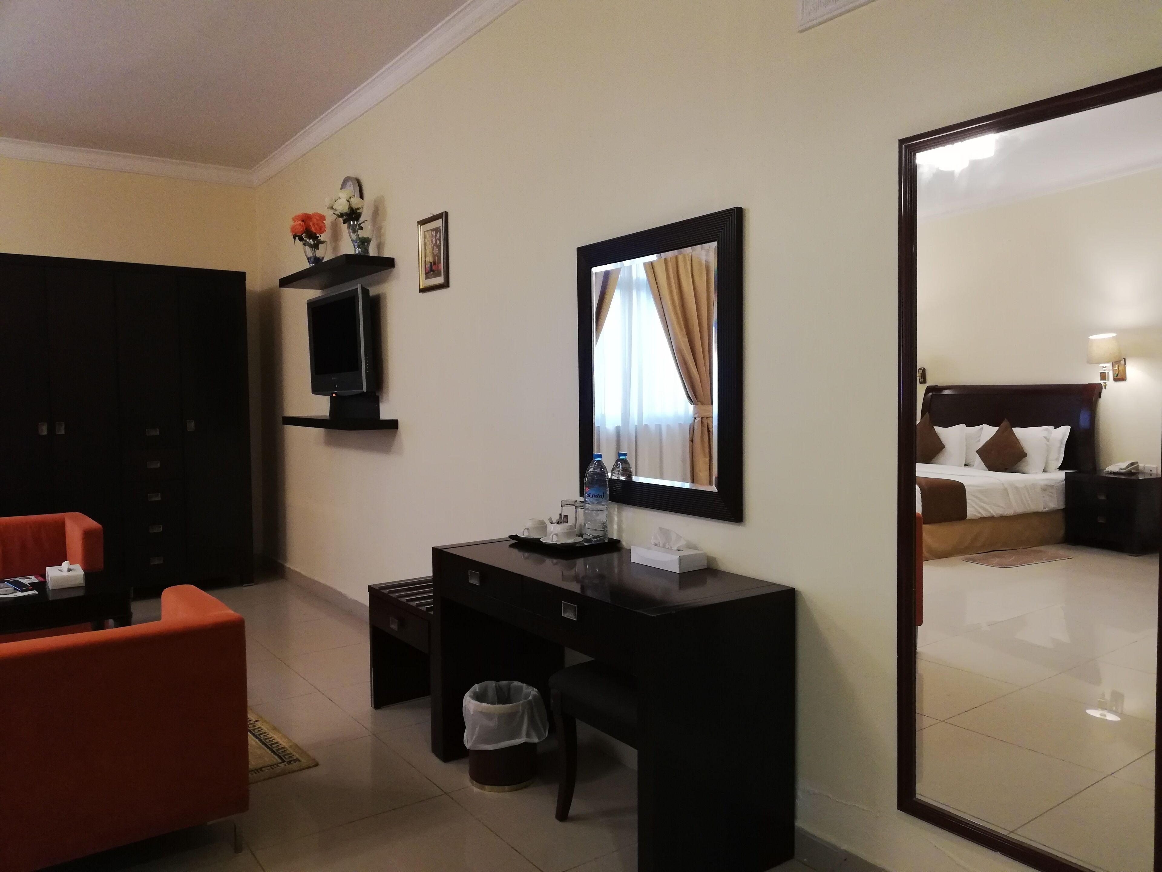 Ein Hotelzimmer mit Schreibtisch, Stuhl, Fernseher, Kleiderschrank und einem großen Spiegel.