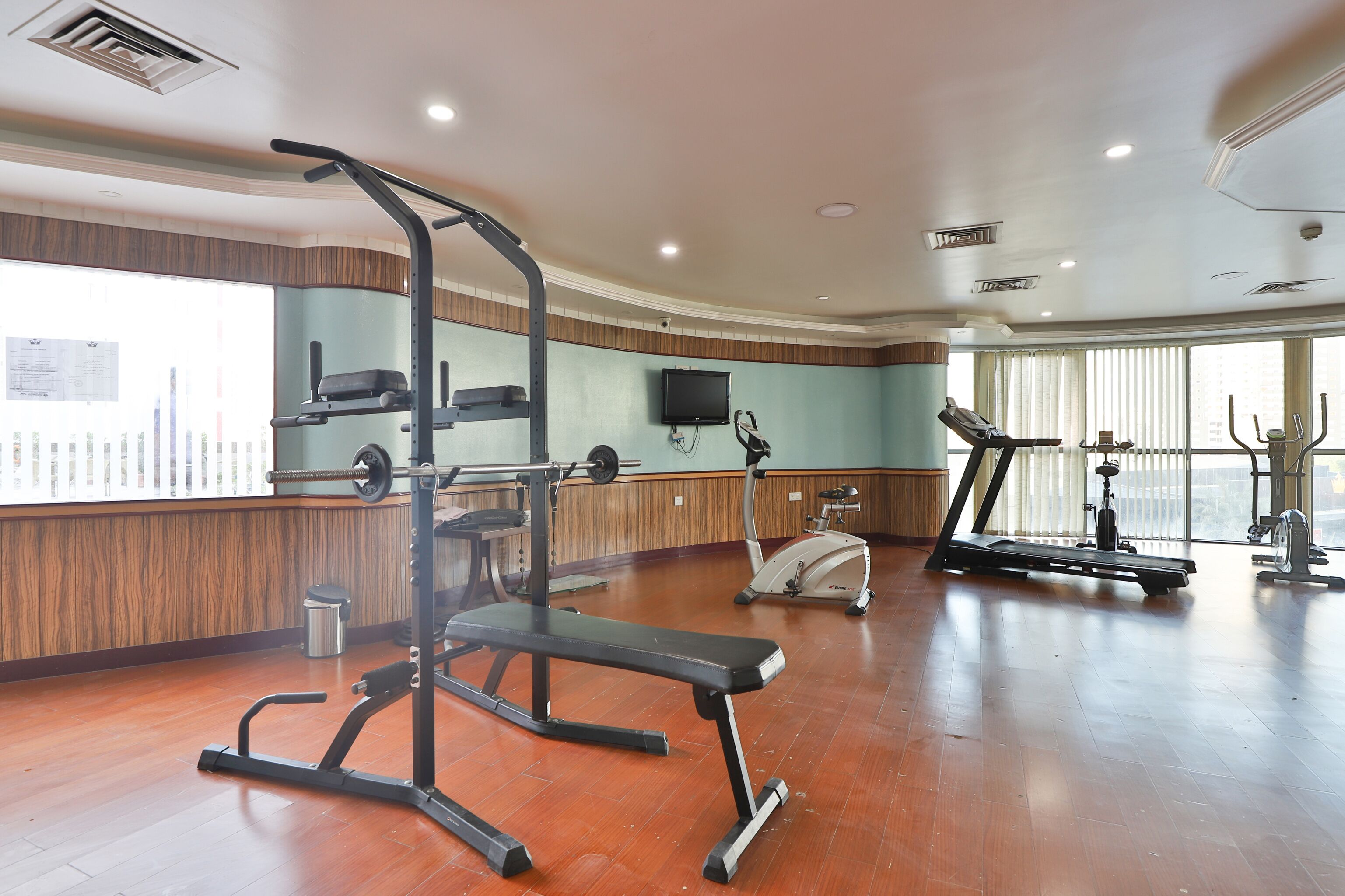 Un gimnasio amplio con diversos equipos de ejercicio, ventanas grandes y suelo de madera.