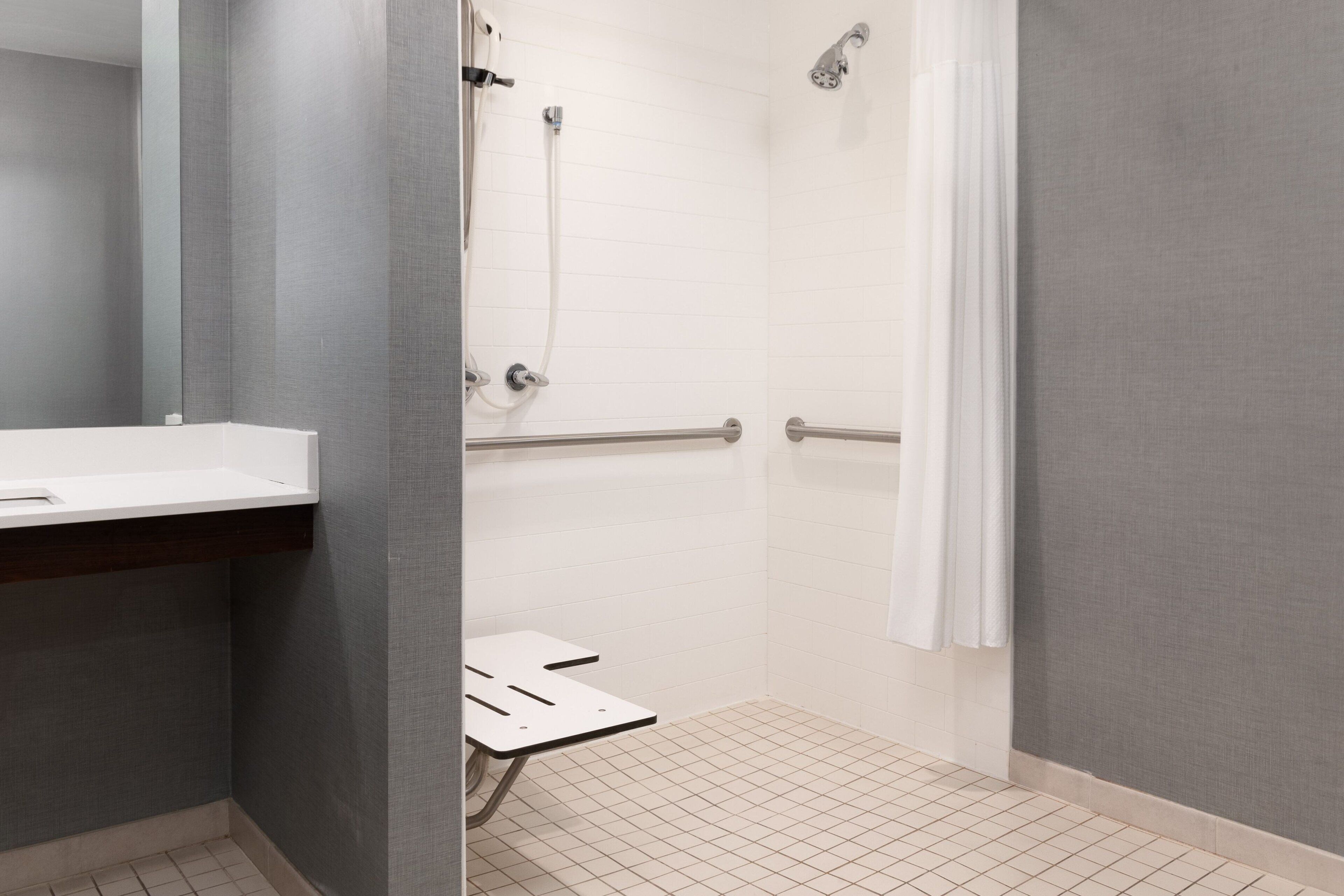 Un baño moderno con un lavamanos blanco, una ducha con puerta de cristal y una barra de apoyo.