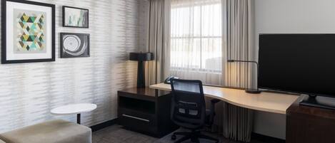 Habitación de hotel con escritorio, una silla, televisor, una mesita y dos cuadros en la pared.