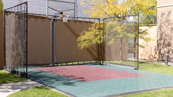 Una cancha de baloncesto con aro, red y superficie de juego verde y roja.