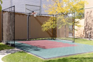 Una cancha de baloncesto con aro, red y superficie de juego verde y roja.