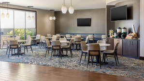 A modern dining area with round tables and chairs, a patterned carpet, and a flat-screen TV mounted on the wall. - Residence Inn Youngstown Warren/Niles (Niles)