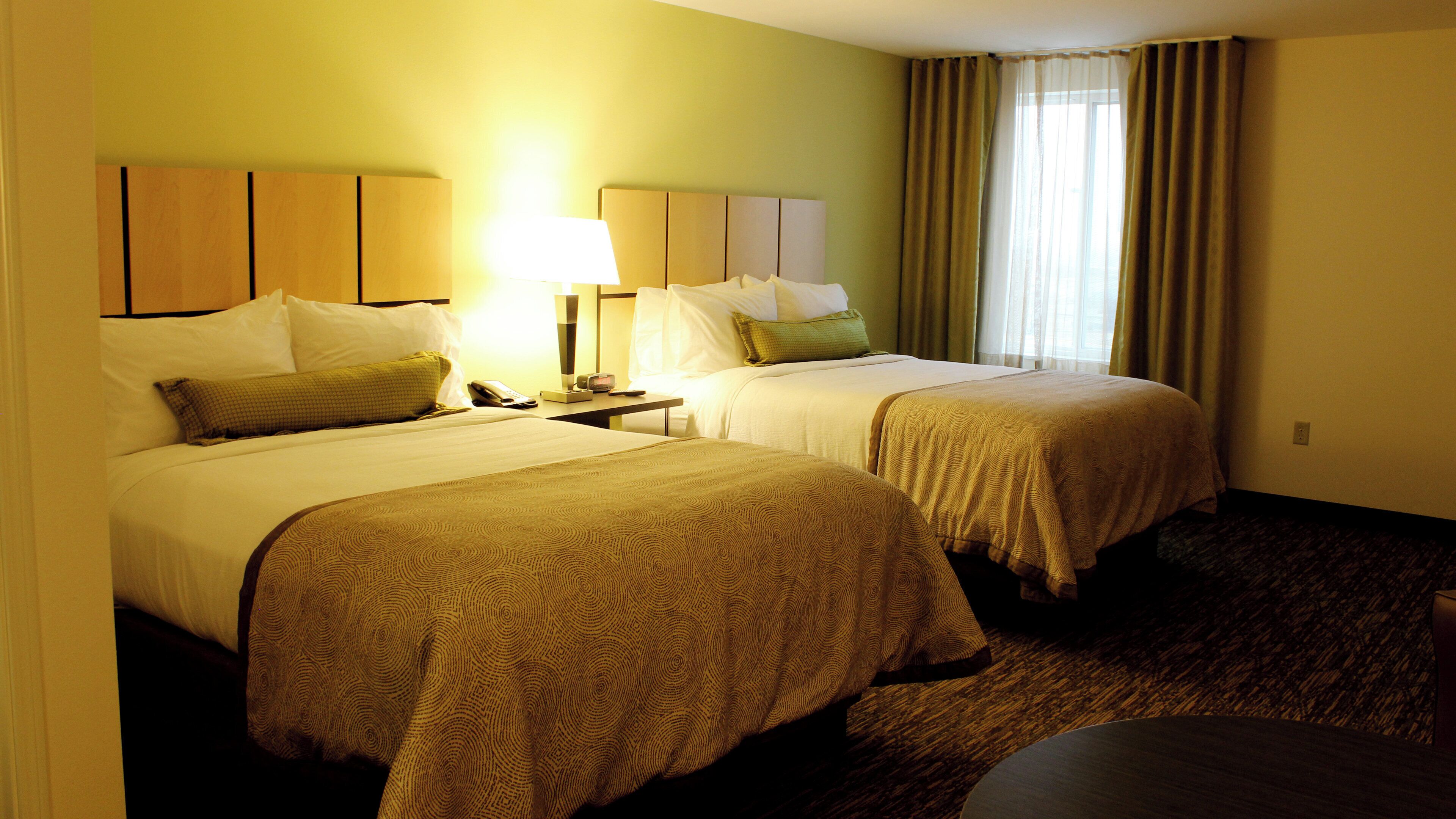 Habitación de hotel con dos camas, una mesita de noche, una lámpara y una ventana con cortinas.