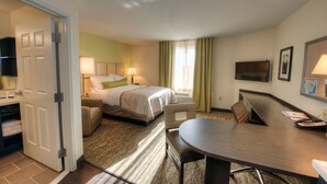 Quarto de hotel com uma cama, escrivaninha, cadeira, televisão e porta.