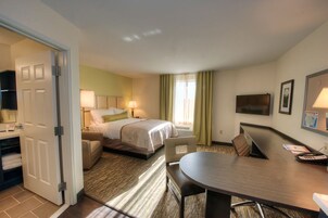 A hotel room with a bed, a desk, a chair, a television, and a door.