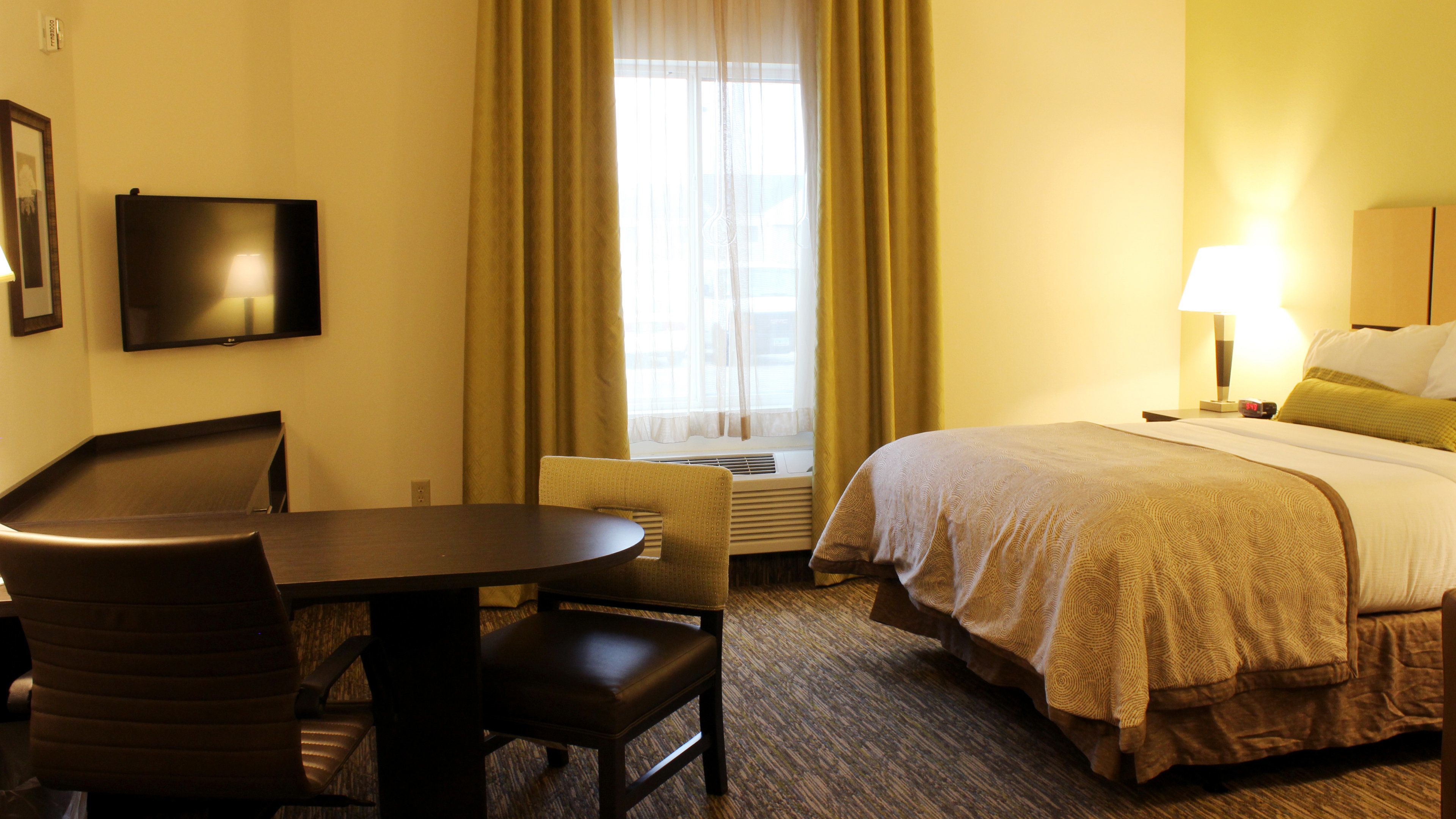 A hotel room with a bed, a desk, a chair, a TV, a window with curtains, and a nightstand with a lamp.