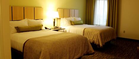 A hotel room with two beds, a bedside table with a lamp, a telephone, and a window with curtains.