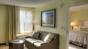 Quarto de hotel com sofá, mesa pequena, cama e quadro na parede.