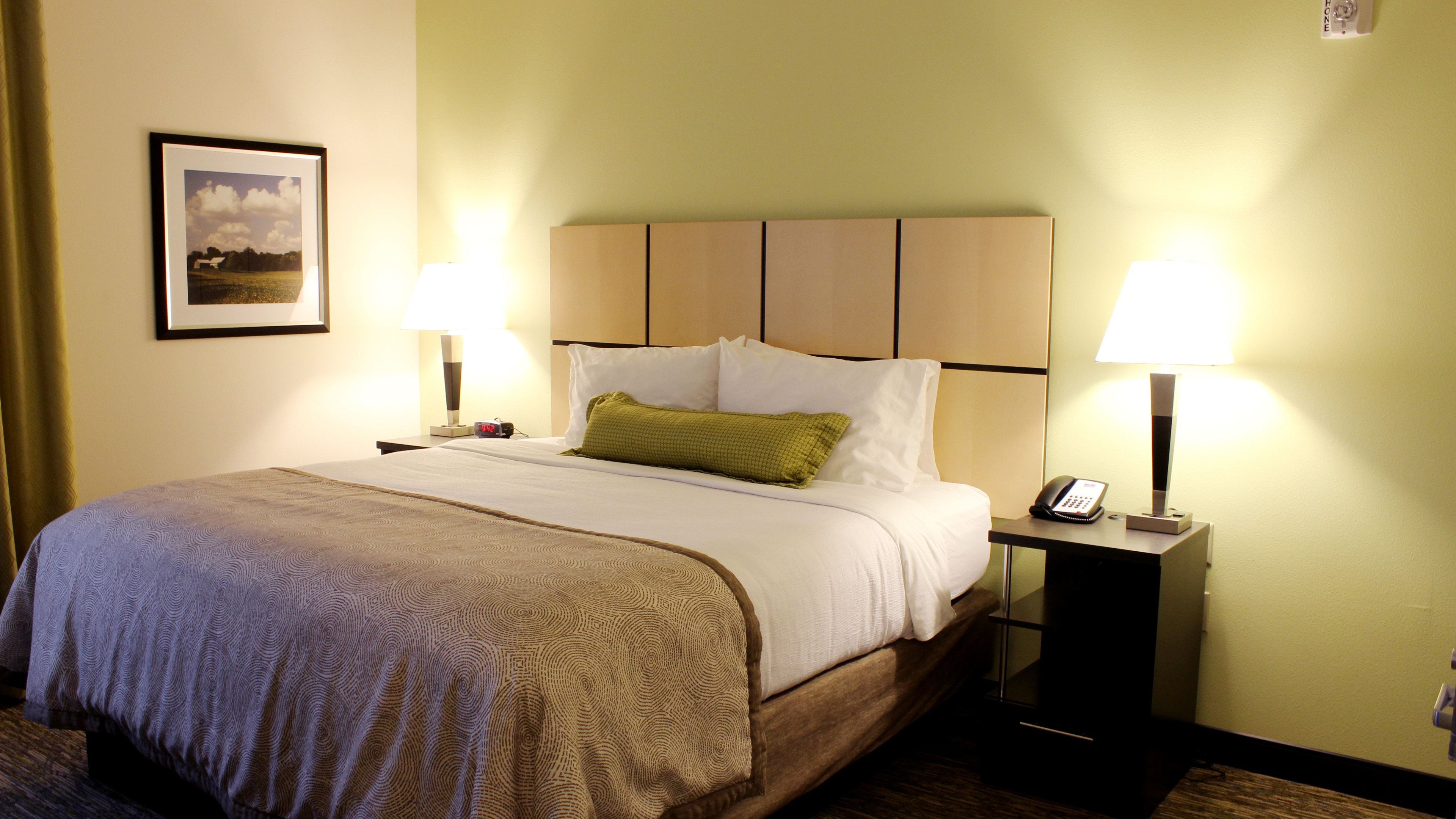 A hotel room with a bed, two bedside tables with lamps, a framed picture on the wall, and a telephone on one of the tables.