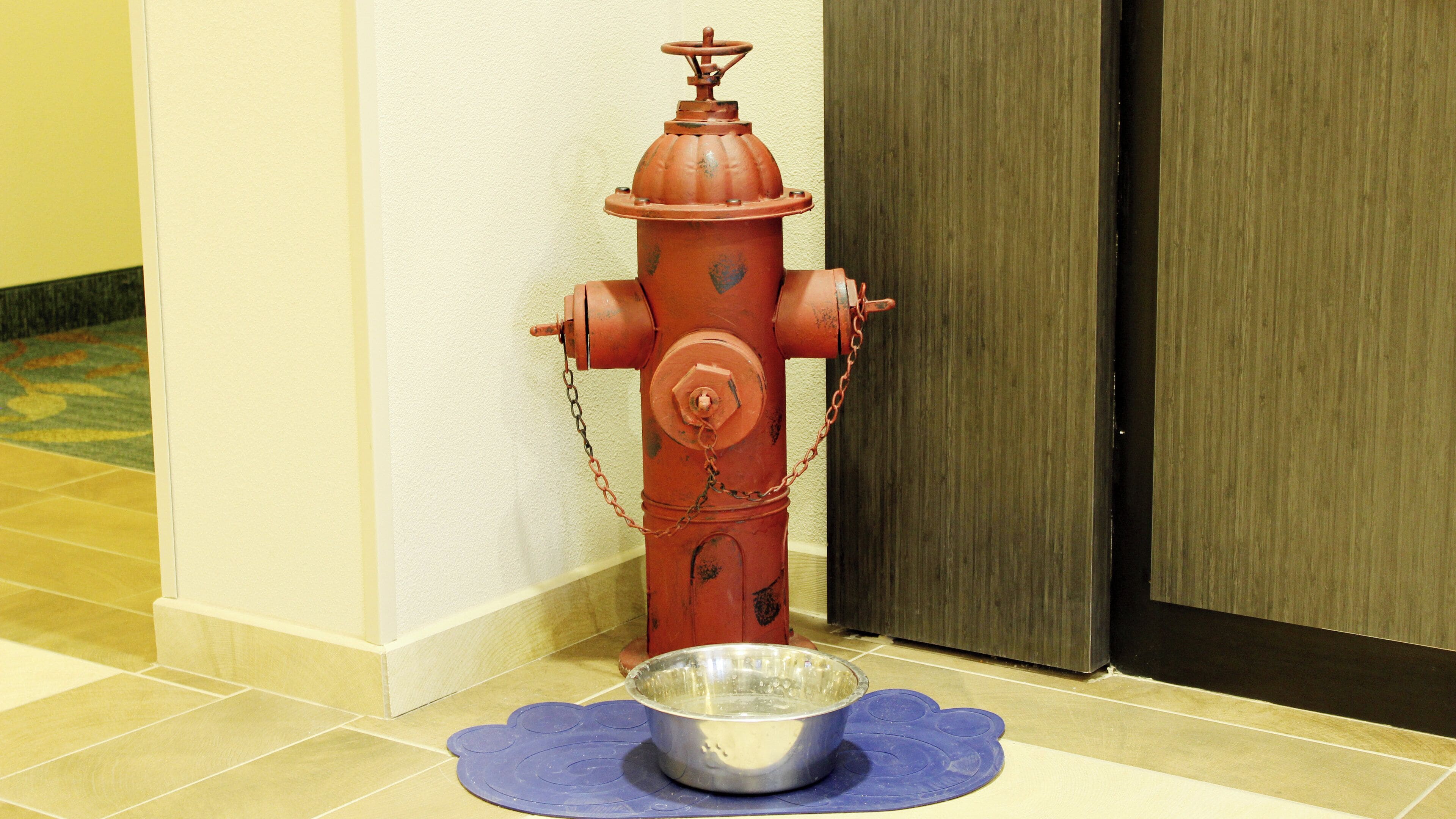 A red fire hydrant next to a door with a blue mat on the floor.