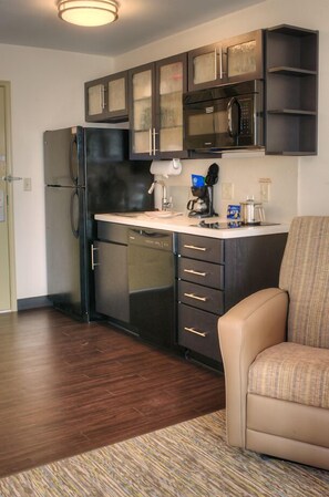 A compact kitchen with dark cabinetry, a built-in microwave, and a refrigerator. - Candlewood Suites Sioux City - Southern Hills by IHG (Sioux City)