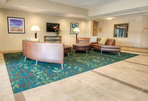 A hotel lobby with a large, colorful carpet, a brown leather sofa, a smaller sofa, and a flat-screen TV on the wall. - Candlewood Suites Sioux City - Southern Hills by IHG (Sioux City)