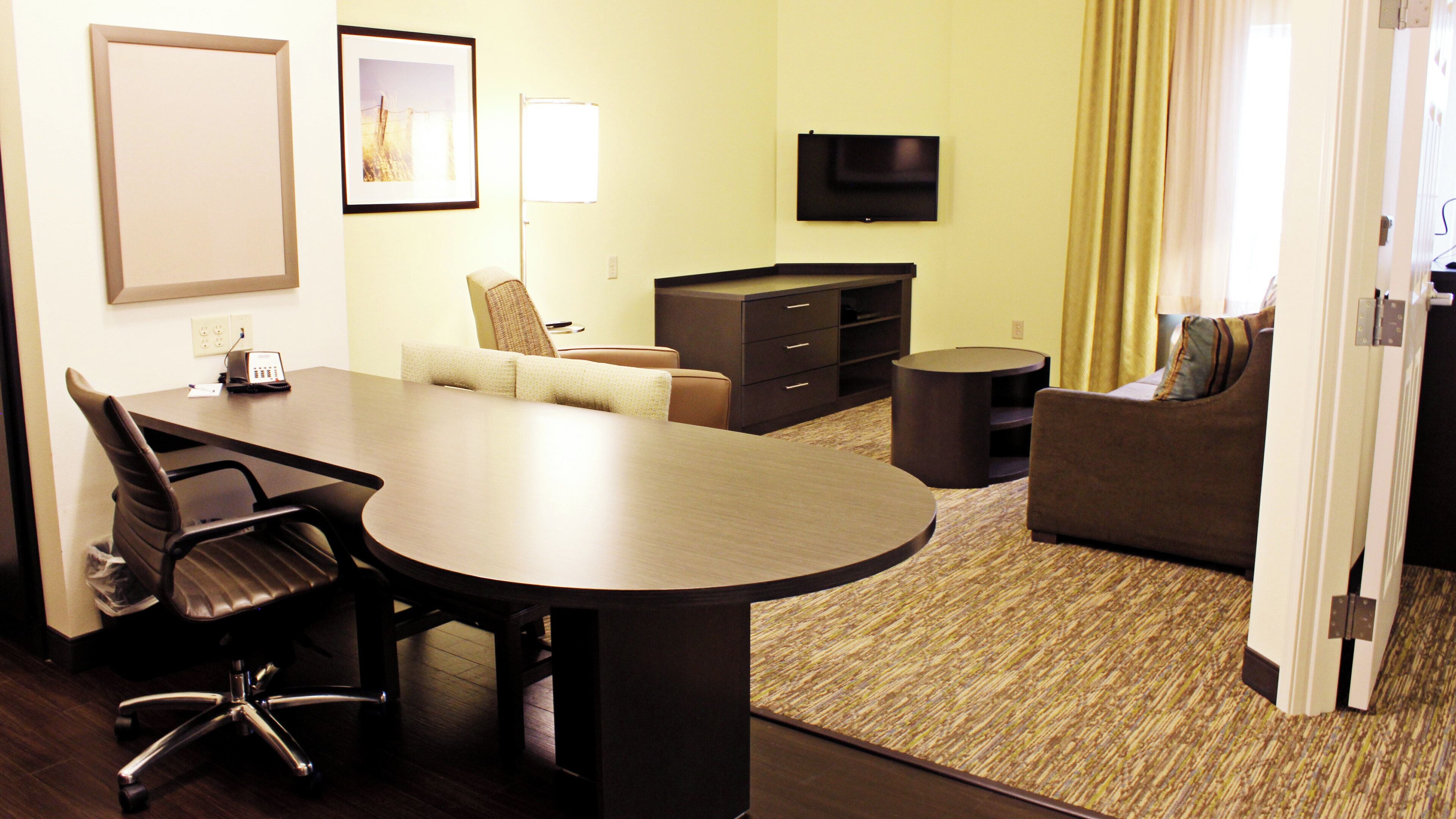 A hotel room with a conference table, a sofa, a TV, and a small round table.