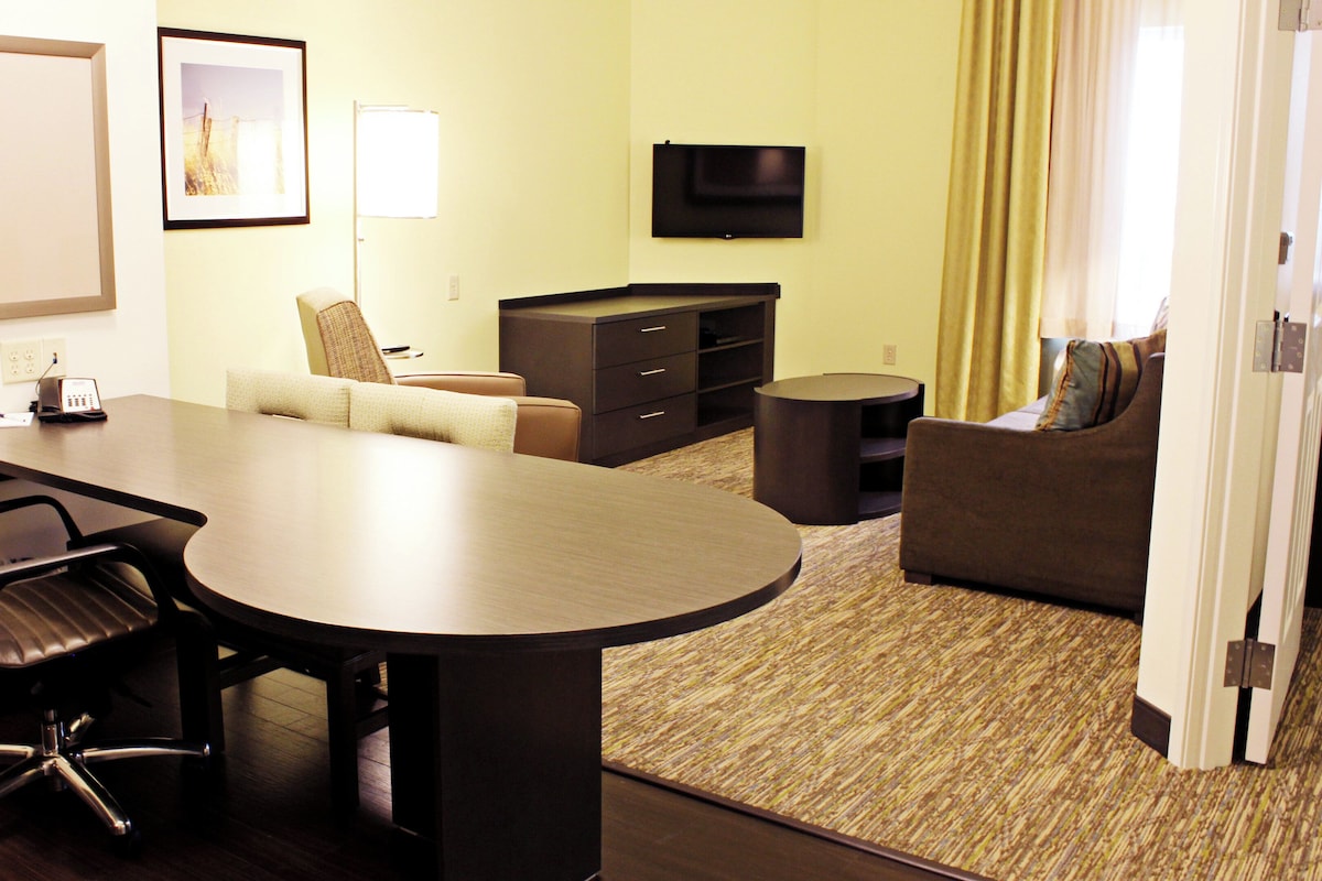 Quarto de hotel com uma mesa de conferências, um sofá, uma TV e uma pequena mesa redonda.