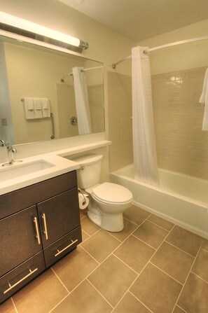 A bathroom with a toilet, sink, vanity, and a shower area. - Candlewood Suites Sioux City - Southern Hills by IHG (Sioux City)