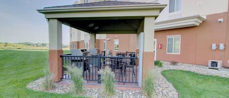 A covered outdoor seating area with a grill, surrounded by a stone border and grass.