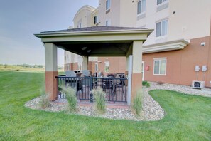 A covered outdoor seating area with a grill, surrounded by a stone border and grass. - Candlewood Suites Sioux City - Southern Hills by IHG (Sioux City)