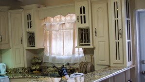 A kitchen with white cabinets, a granite countertop, and a window with sheer curtains. - Hopeville Apartments (Charnocks)