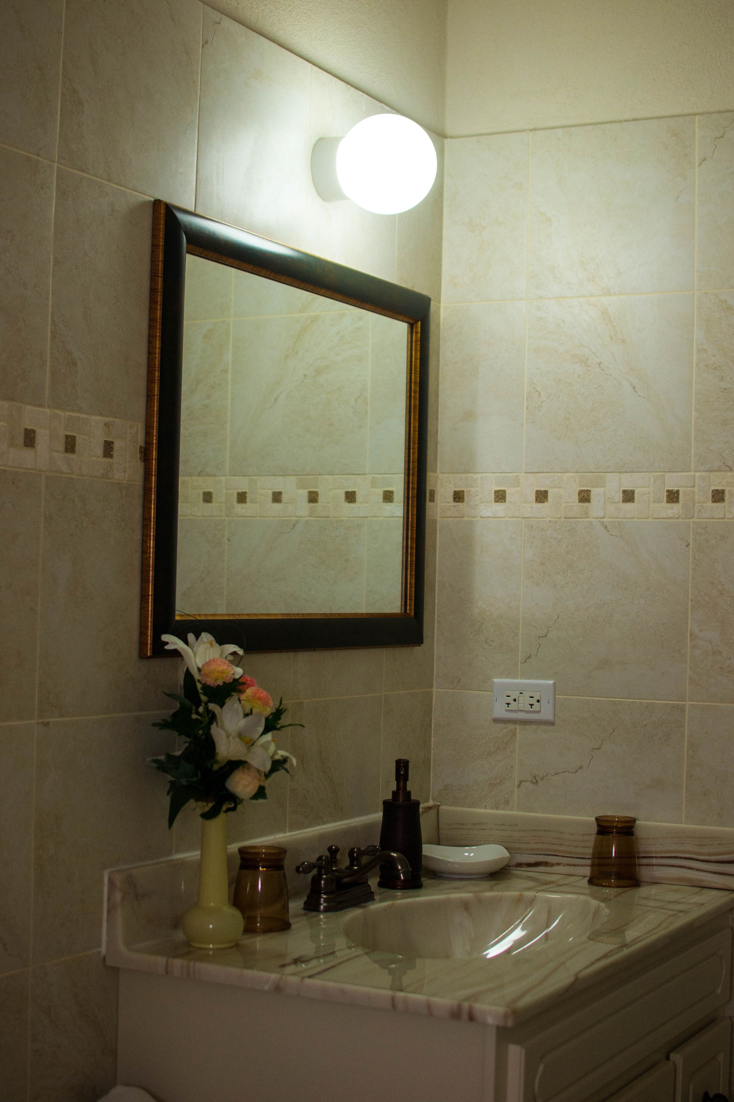 Un baño con un lavamanos de mármol, un espejo con marco dorado y un florero con flores.