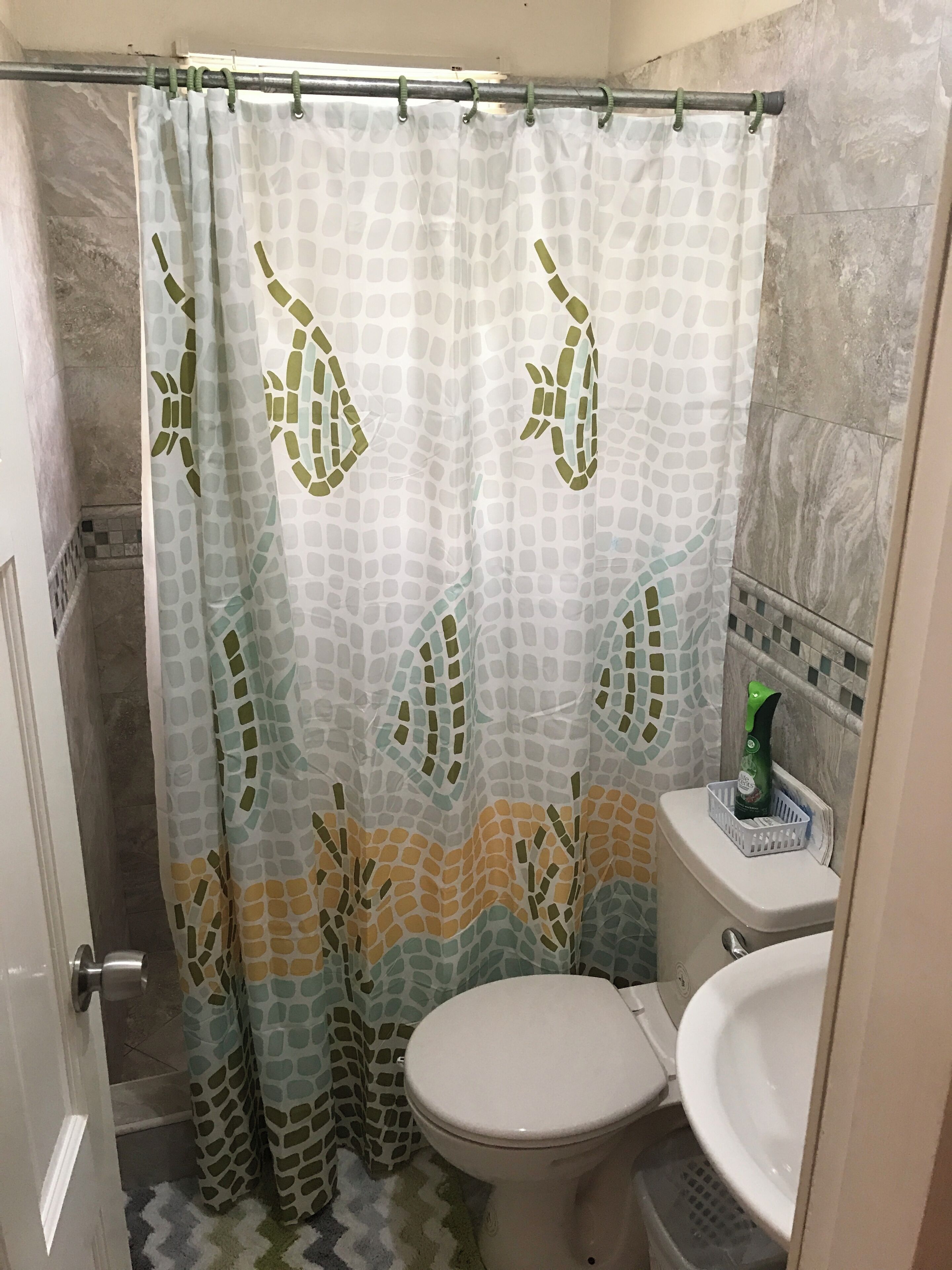 A bathroom with a shower curtain featuring a leaf pattern, a toilet, and a sink.