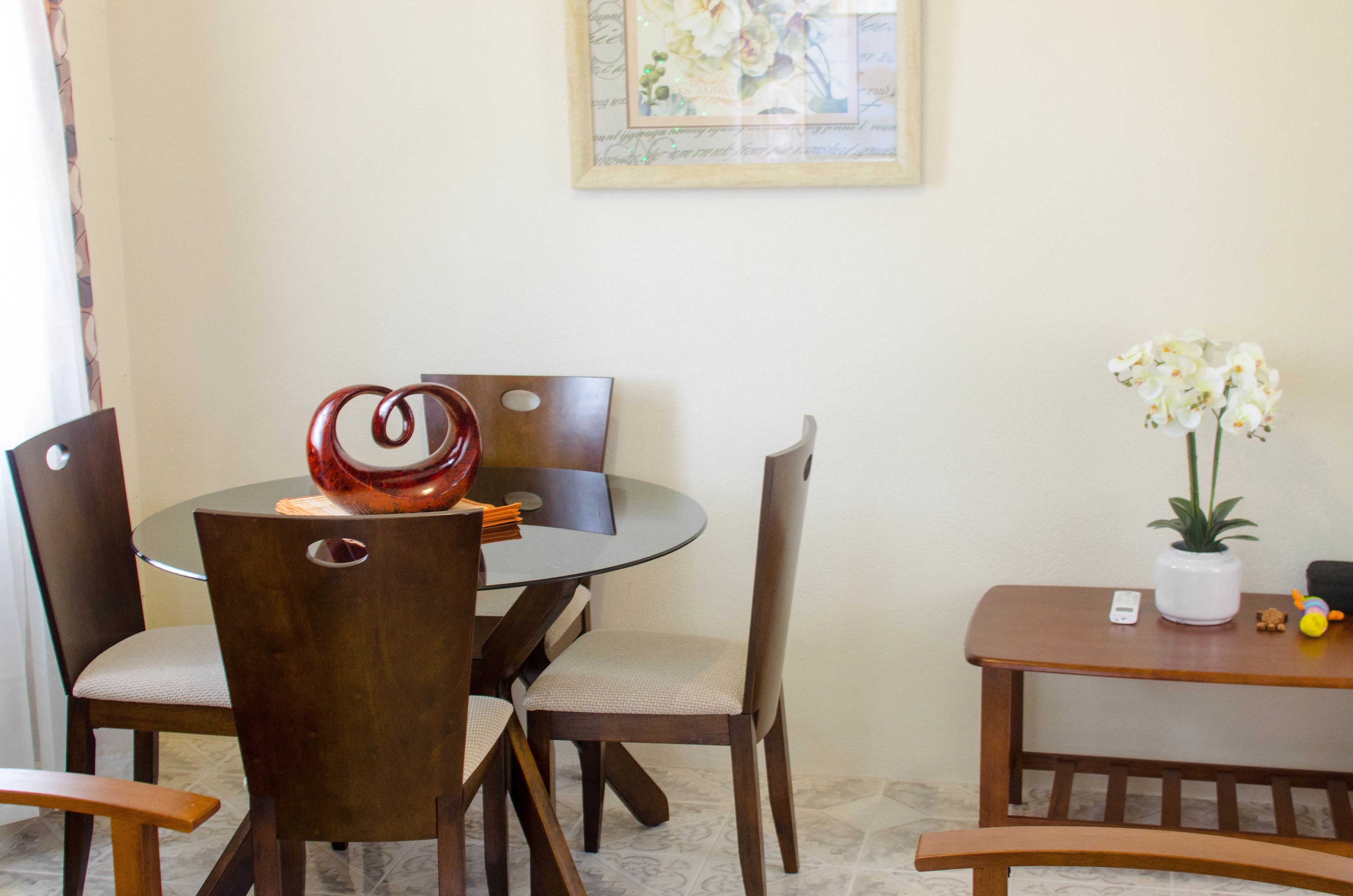 Un coin repas comprenant une table ronde, quatre chaises, un vase avec des fleurs et une petite table sur laquelle sont posés une plante et un jouet.