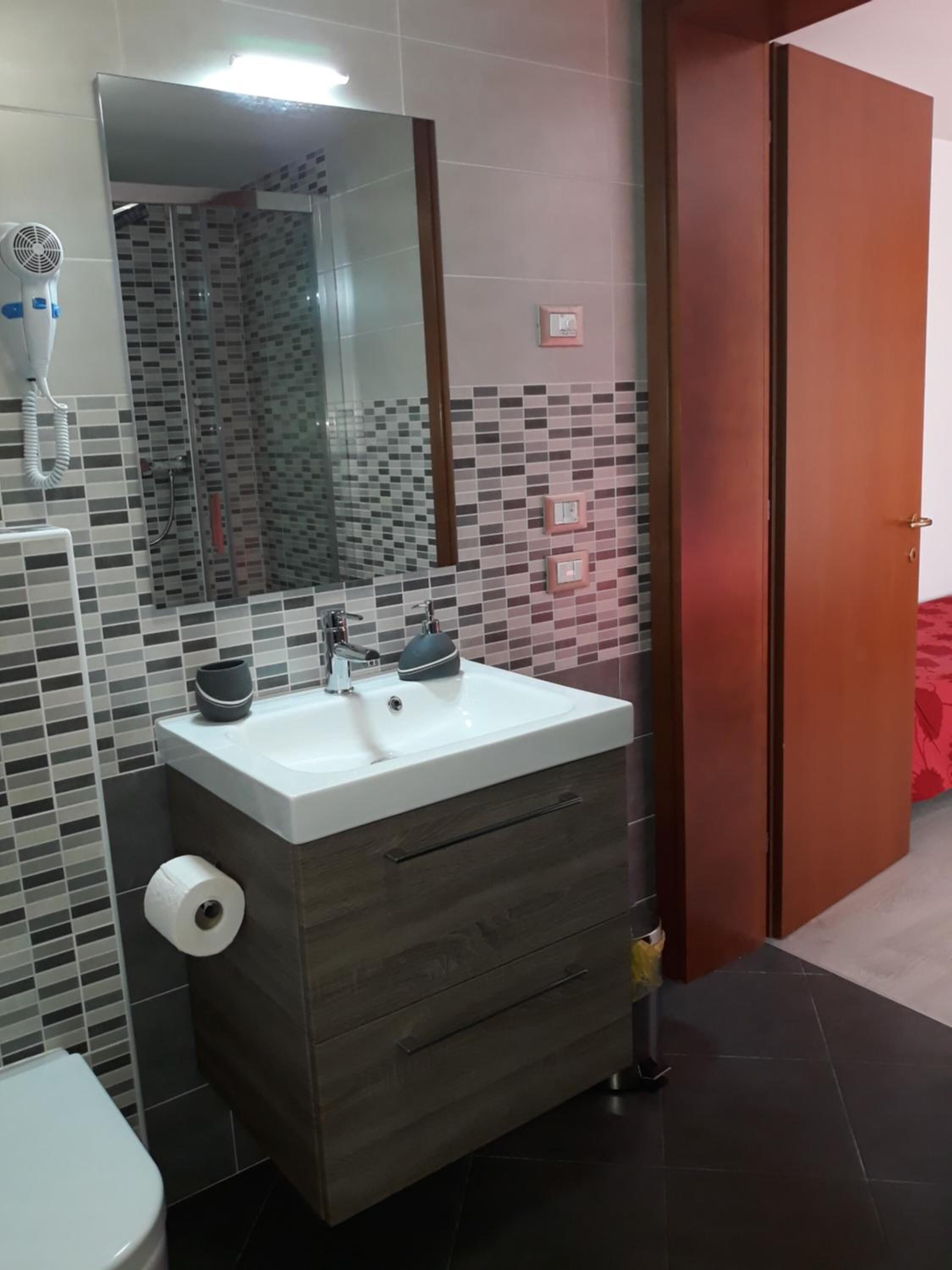 Un bagno con un lavandino bianco, un mobile contenitore in legno scuro e uno specchio.