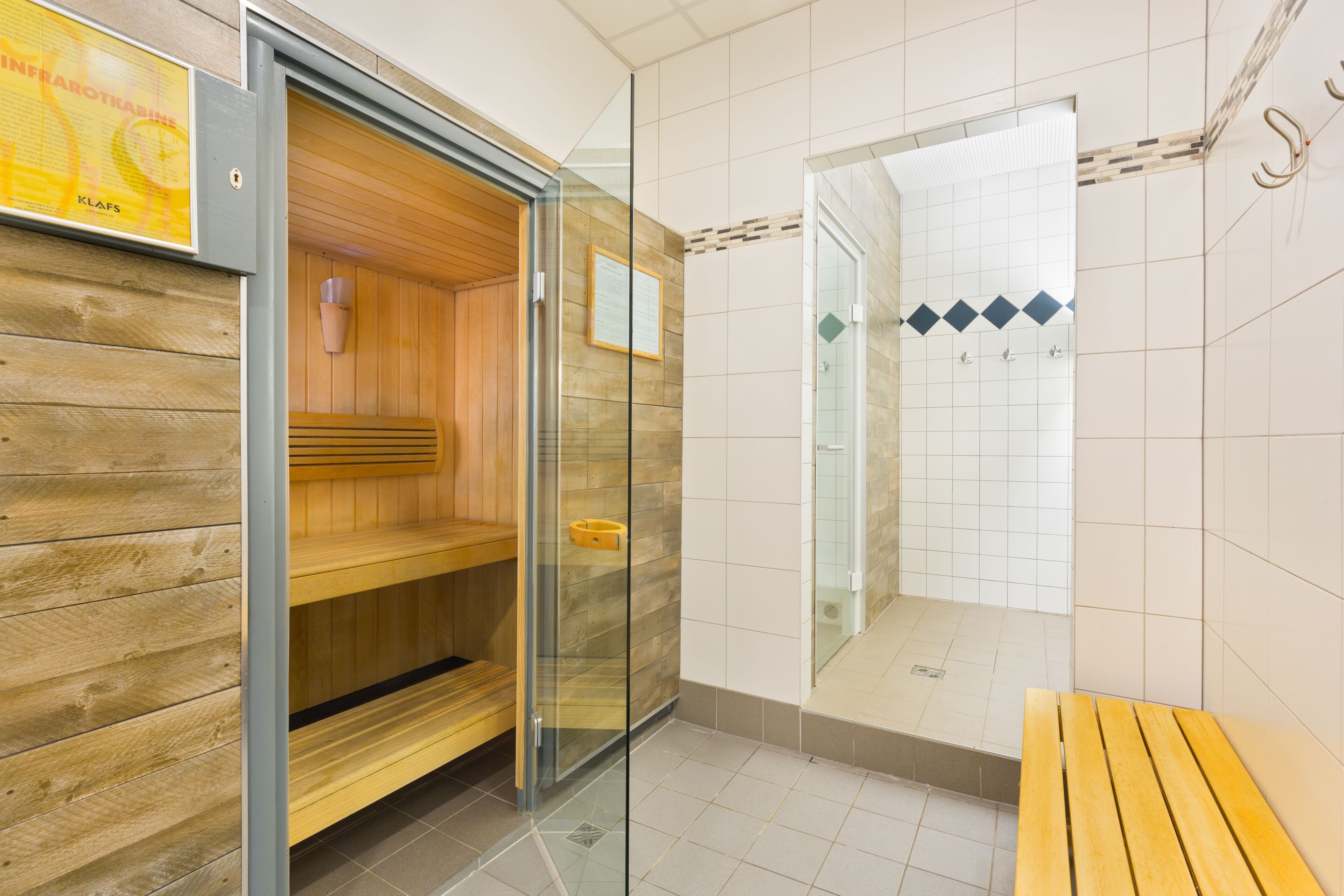 Ein Sauna-Raum mit Holzbänken, einer Glastür und einem gefliesten Duschbereich.