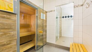 Ein Sauna-Raum mit Holzbänken, einer Glastür und einem gefliesten Duschbereich.
