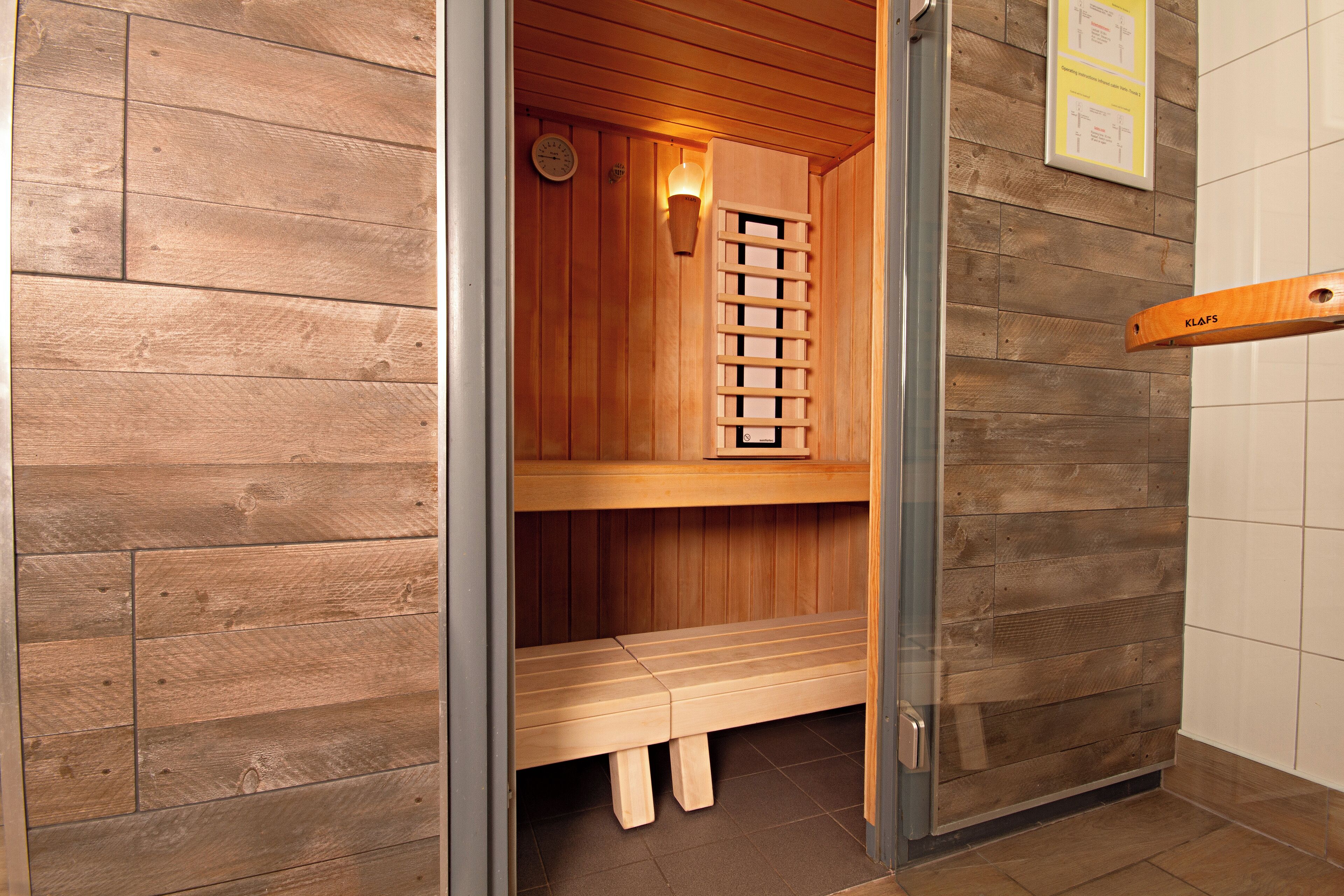 Eine Sauna mit Holzwänden und -bänken, einer Wanduhr und einer Saunatür.
