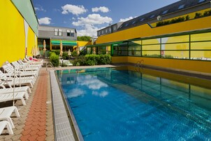 A swimming pool with sun loungers and umbrellas, surrounded by buildings with large windows.