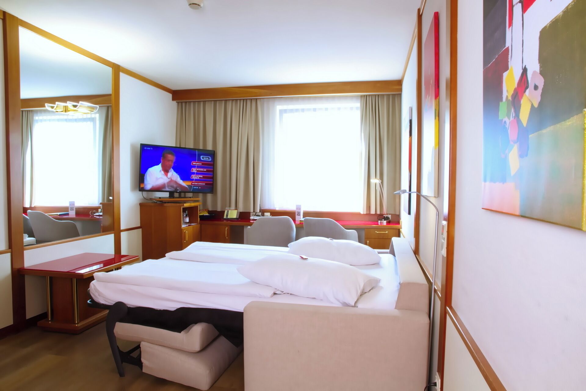 Una habitación de hotel con cama, escritorio, televisión y un espejo grande.