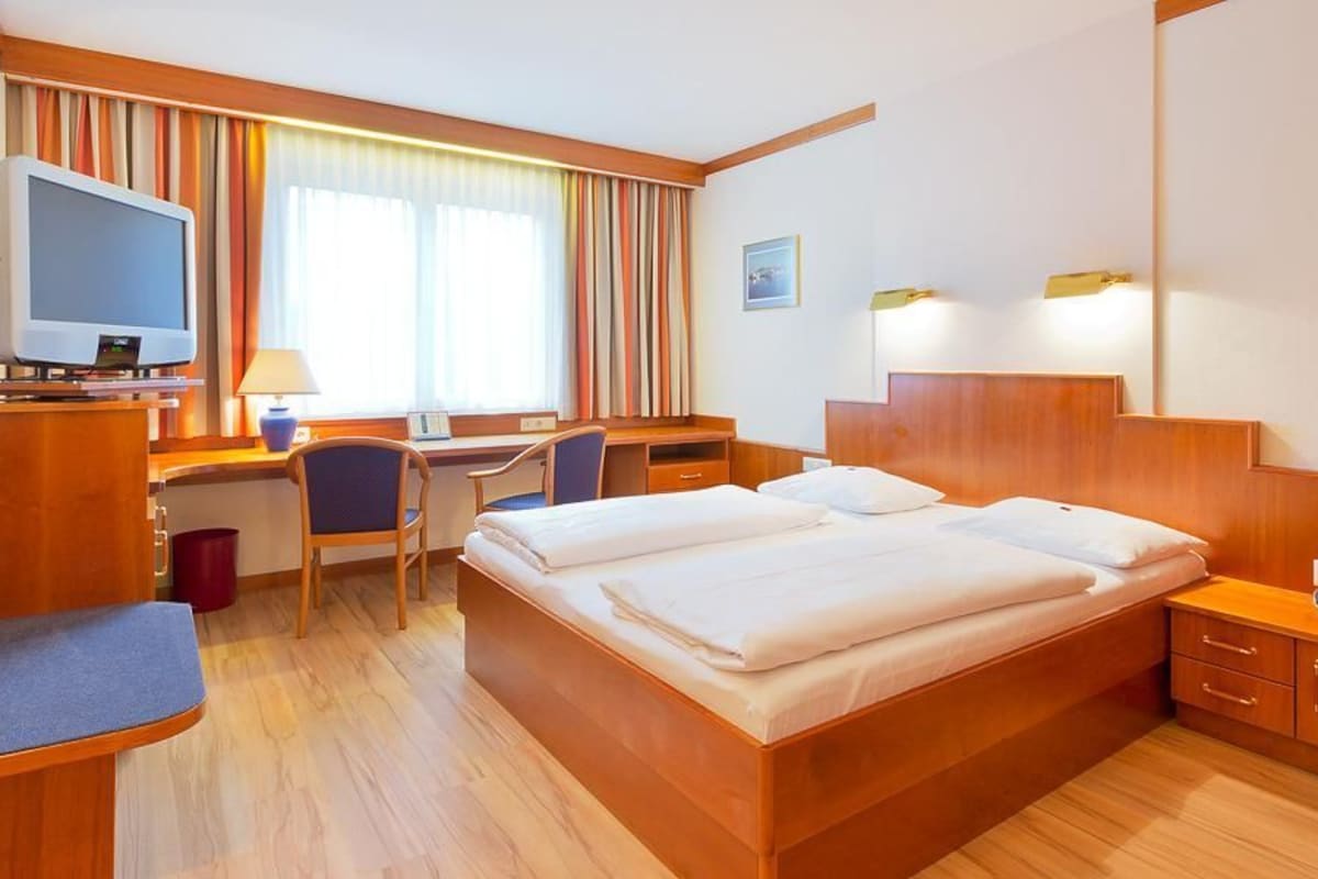 Ein Hotelzimmer mit einem Bett, einem Schreibtisch mit Computer, einem Fernseher und einer kleinen Sitzecke.