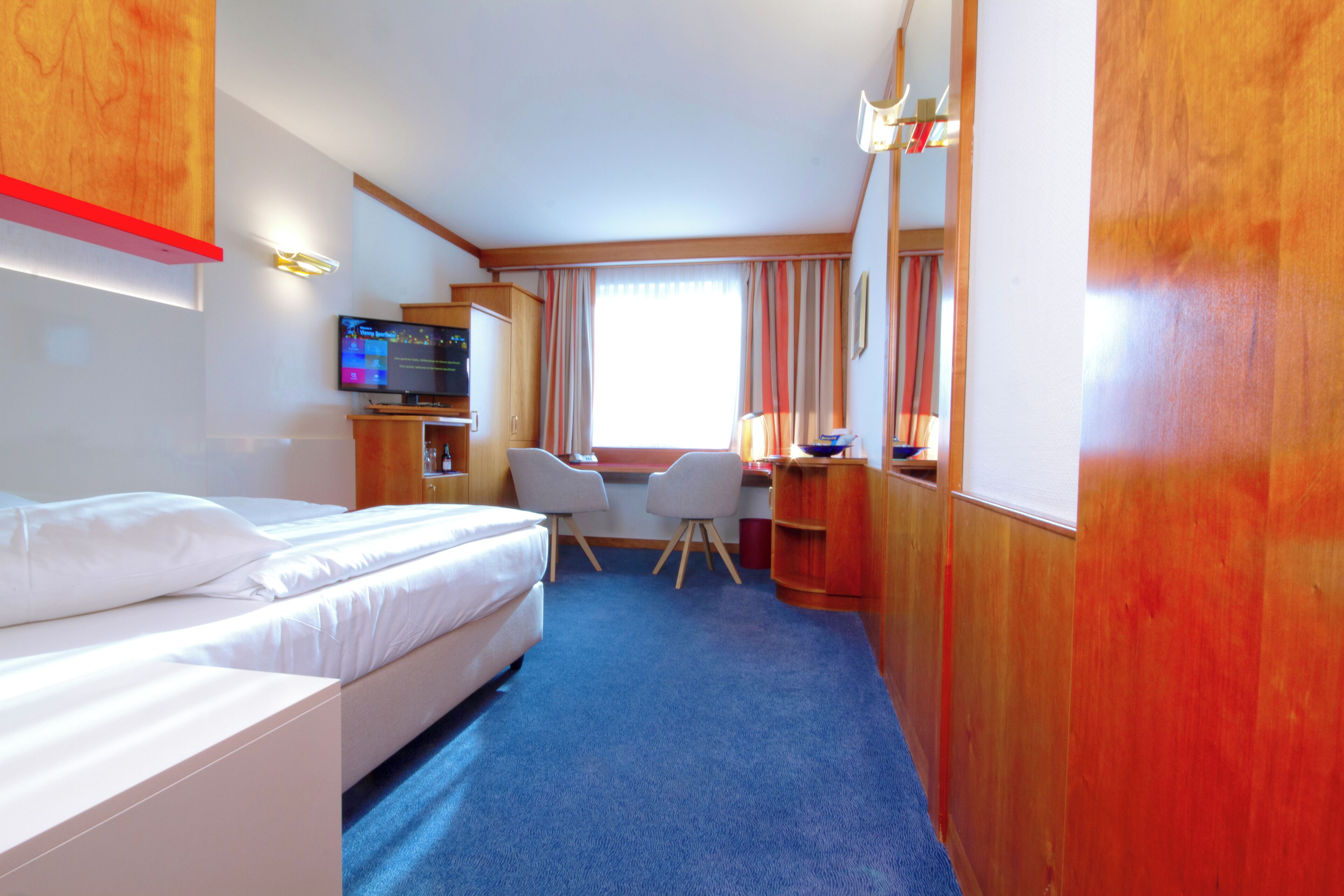 Ein Hotelzimmer mit einem Bett, einem Schreibtisch mit Stuhl, einem Fernseher und einem Fenster mit Vorhängen.