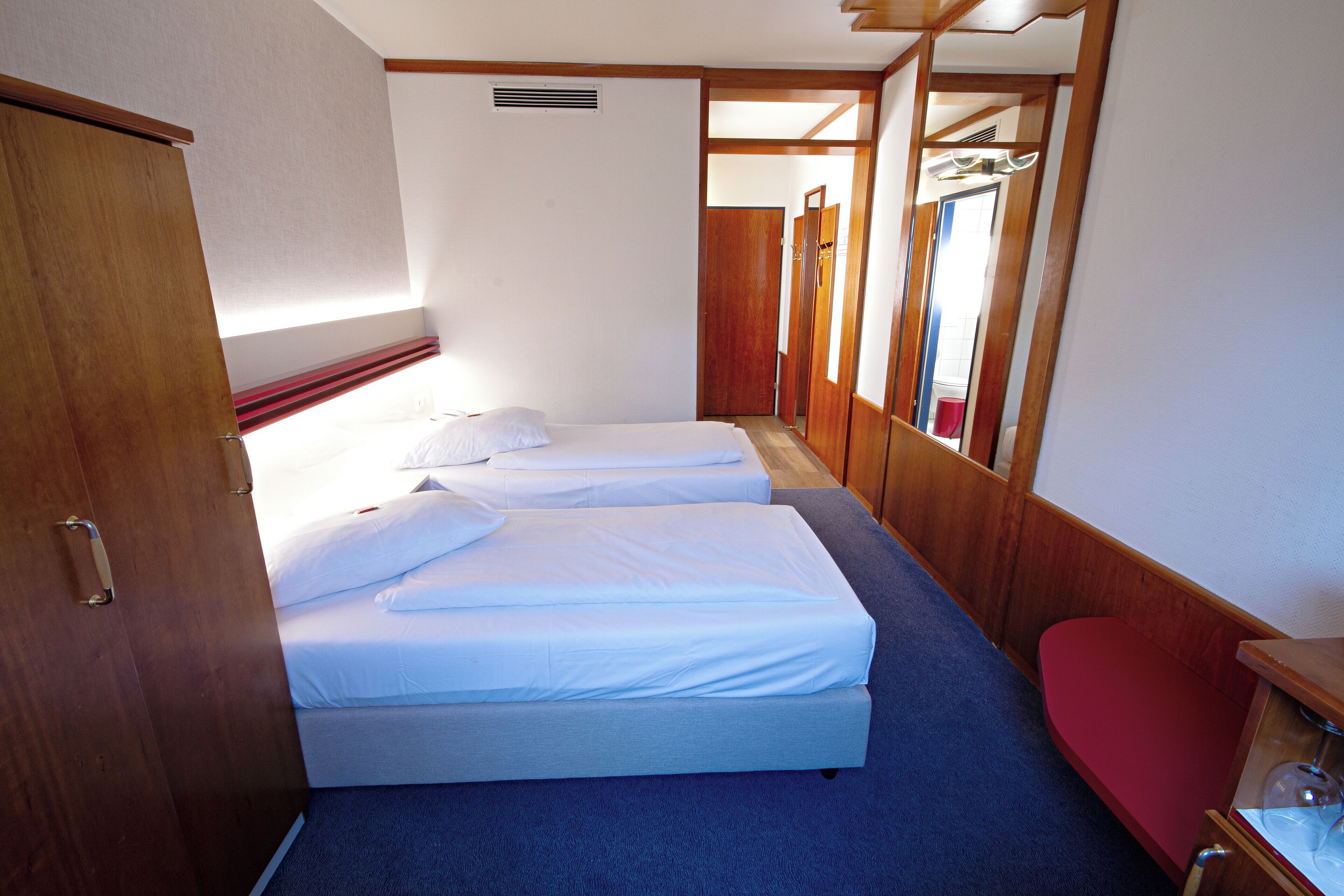 Un dormitorio con dos camas, un armario de madera y una silla roja.