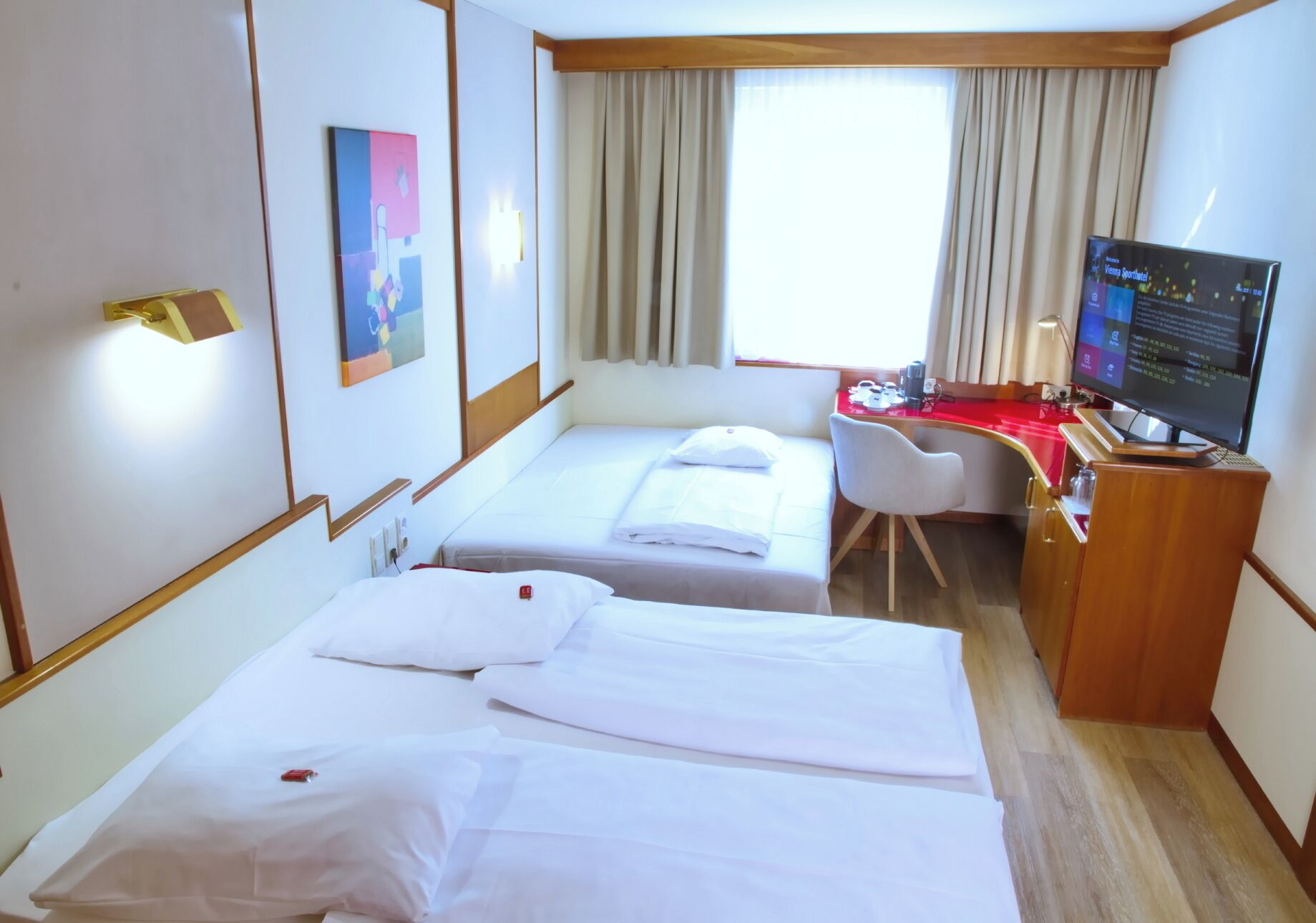 A hotel room with two beds, a desk, a television, and a window with curtains.