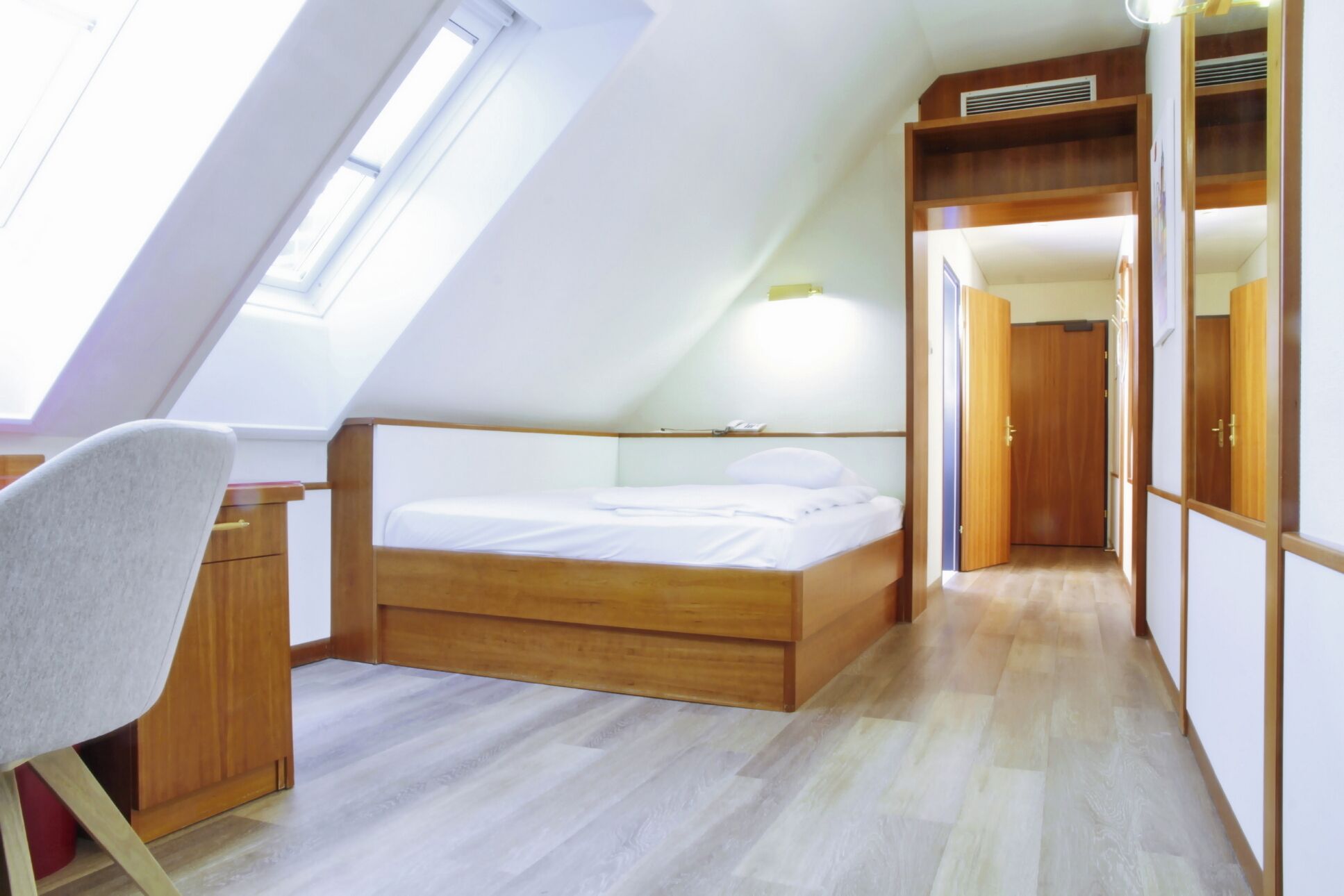Ein Schlafzimmer mit schrägem Dach, einem Bett, einem Schreibtisch und einem Kleiderschrank.
