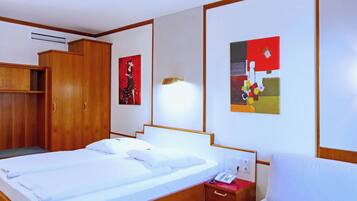 Una habitación de hotel con cama, un armario de madera, una mesita de noche con teléfono y dos cuadros en la pared.