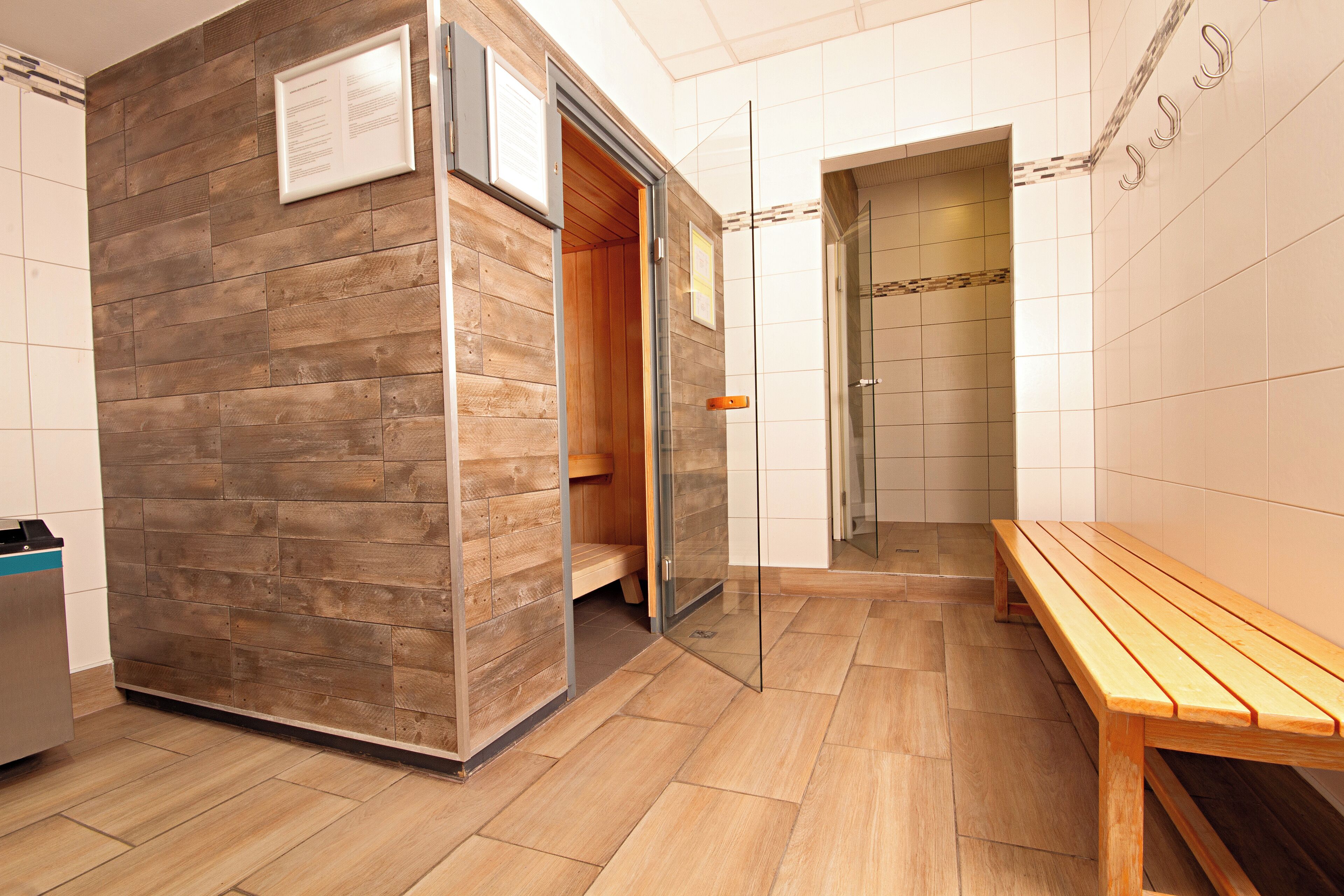 Ein Saunaraum mit Holzwänden, einer Sitzbank und einer Glastür zu einem Duschbereich.
