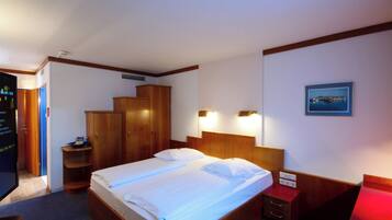 Habitación de hotel con cama, armario de madera, mesita de noche y un cuadro en la pared.