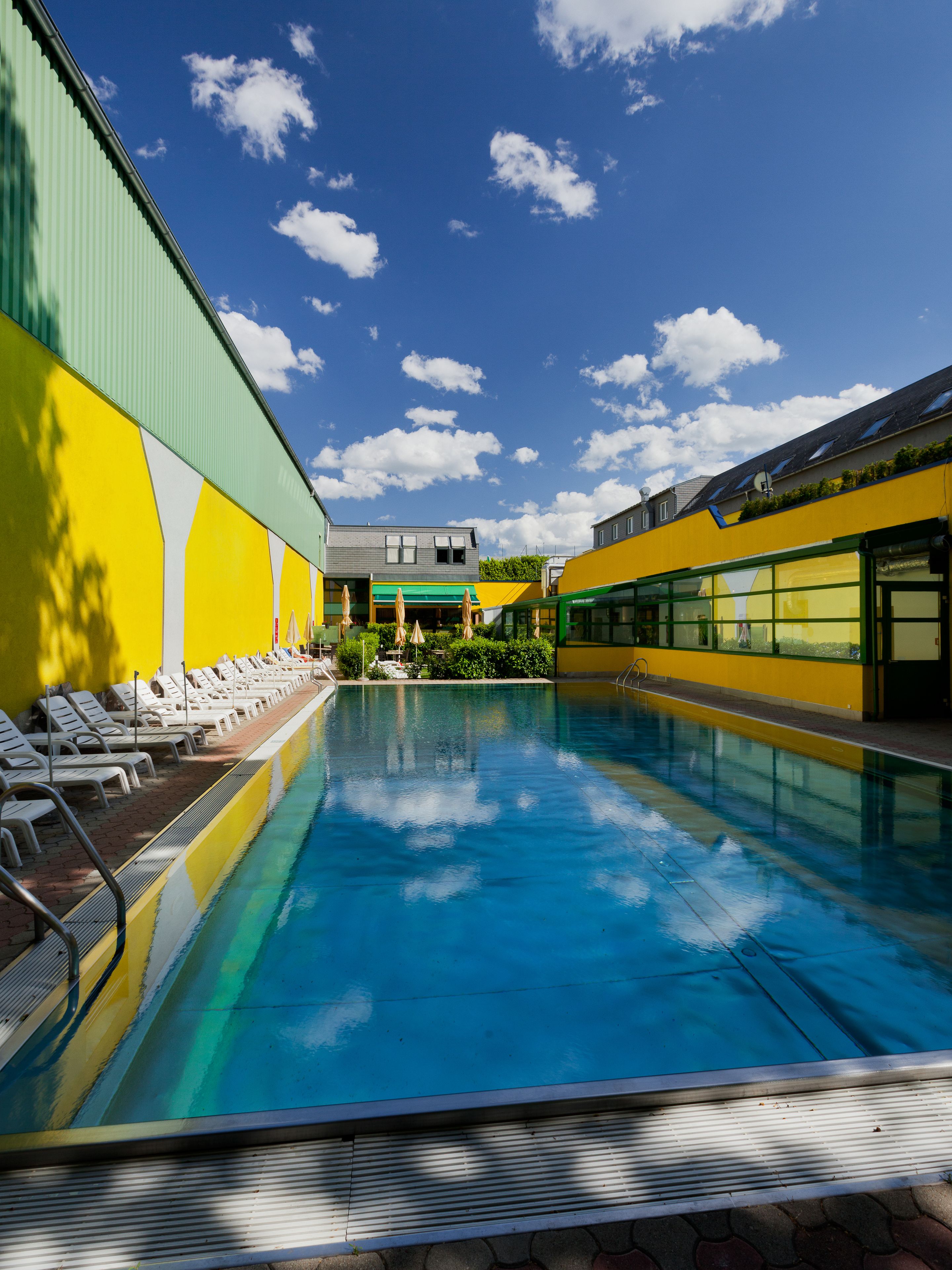 Une piscine avec des chaises longues et un bâtiment aux murs verts et jaunes.