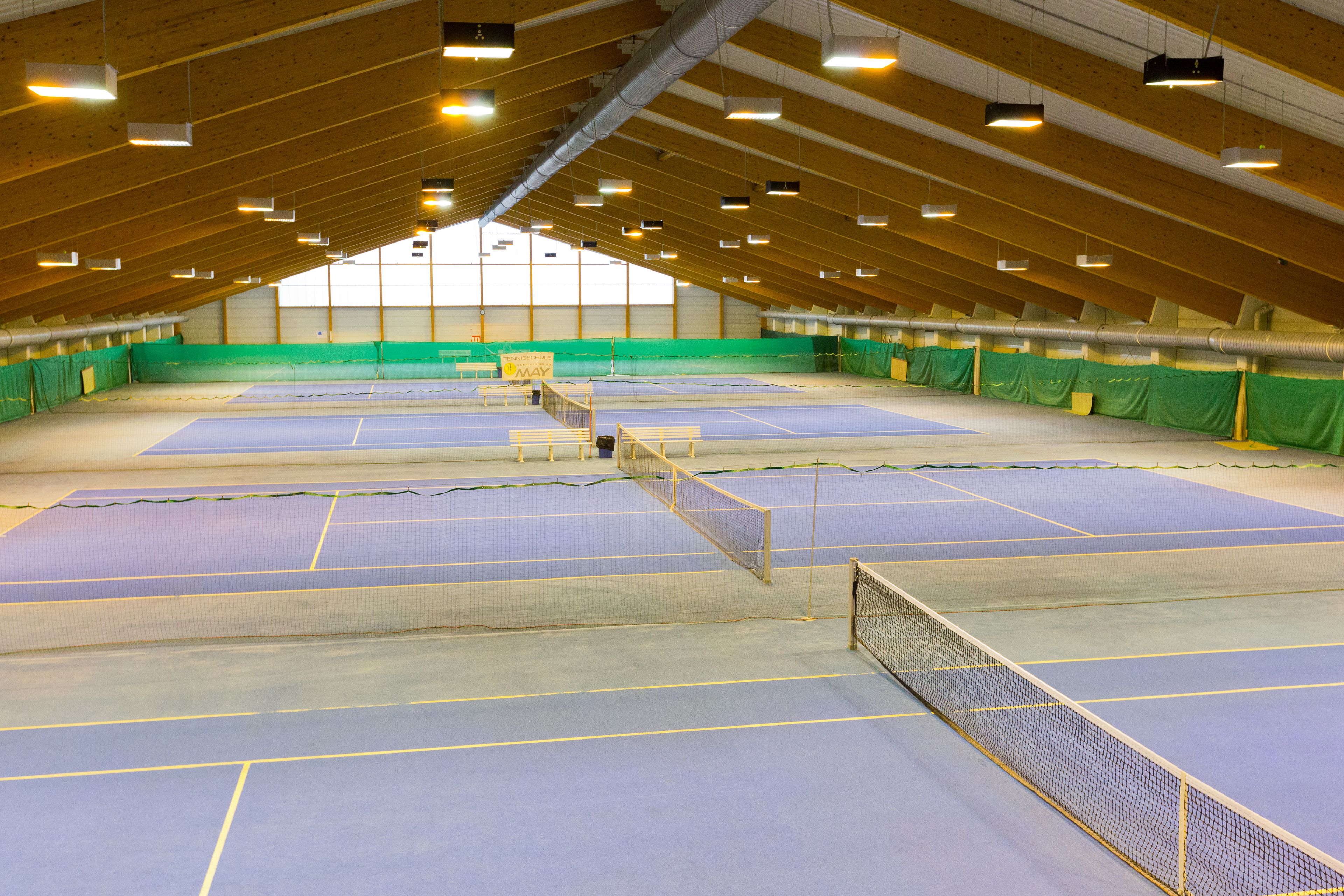 An indoor tennis court with multiple courts, wooden beams, and green curtains.