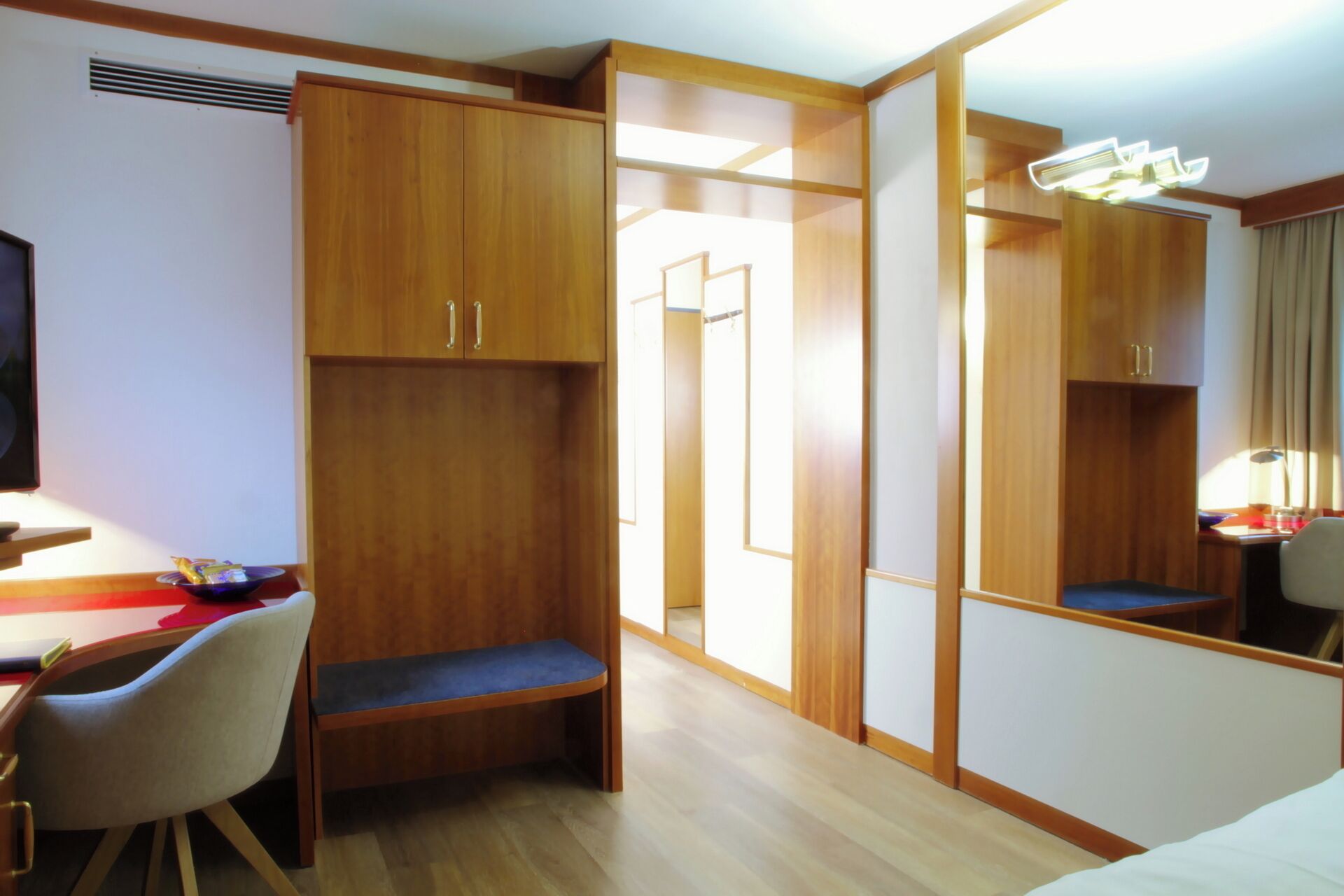 Una habitación de hotel con muebles de madera, un escritorio, una silla, una cama y un espejo.