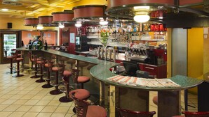 Zona de bar con varios taburetes, una barra con periódicos y una variedad de botellas y vasos en estantes.